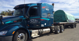 Flatbed truck transporting construction materials with properly secured straps.