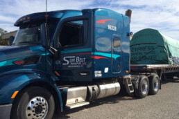 Flatbed truck transporting construction materials with properly secured straps.