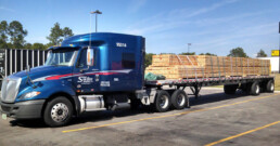 Flatbed truck carrying large wooden beams securely fastened.