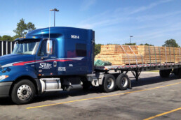 Flatbed truck carrying large wooden beams securely fastened.