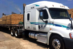 Sunbelt Transport flatbed truck loaded with lumber, secured with straps.